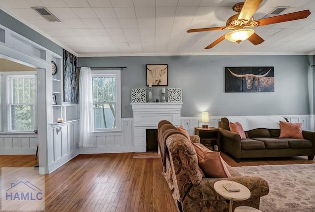 living room with visible vents, crown molding, a wainscoted wall, a fireplace, and hardwood / wood-style flooring