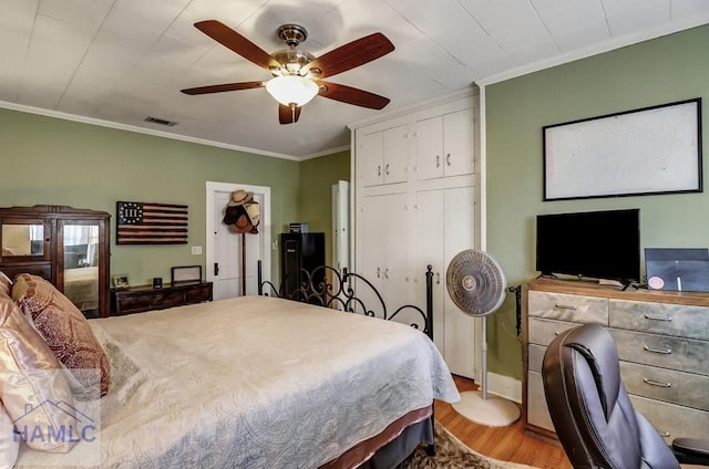 bedroom featuring a ceiling fan, visible vents, light wood finished floors, a closet, and crown molding