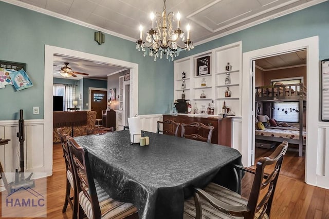 dining room featuring wainscoting, wood finished floors, crown molding, and ceiling fan with notable chandelier