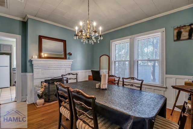 dining space with a wainscoted wall, ornamental molding, a fireplace, an inviting chandelier, and wood finished floors