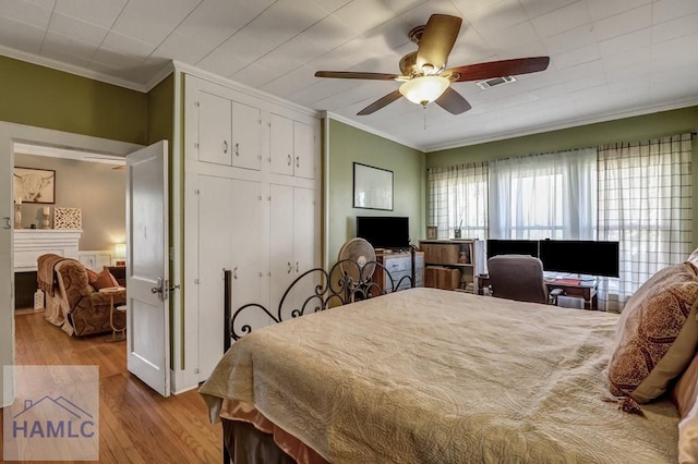 bedroom featuring wood finished floors, a ceiling fan, a fireplace, a closet, and crown molding