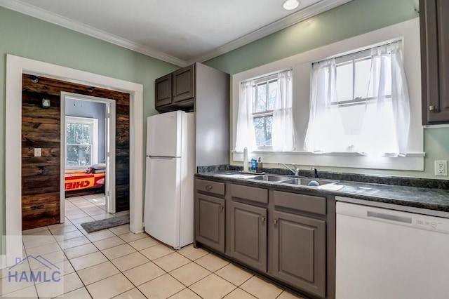 kitchen with white appliances, light tile patterned floors, dark countertops, a sink, and crown molding