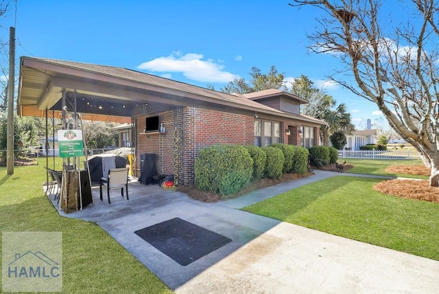 view of property exterior featuring brick siding, a lawn, driveway, and fence