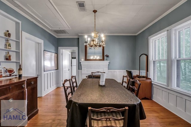 dining room with light wood-style flooring, a fireplace, visible vents, and wainscoting