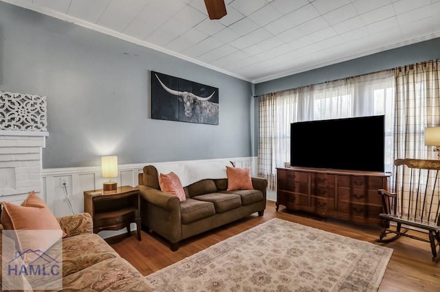 living area featuring wainscoting, ornamental molding, a fireplace, and wood finished floors