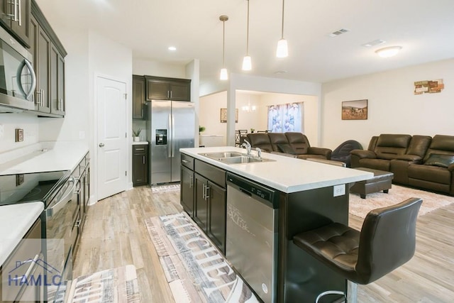 kitchen featuring light wood-type flooring, stainless steel appliances, sink, a center island with sink, and an inviting chandelier