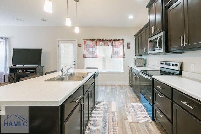 kitchen featuring a center island with sink, hanging light fixtures, sink, light hardwood / wood-style flooring, and appliances with stainless steel finishes