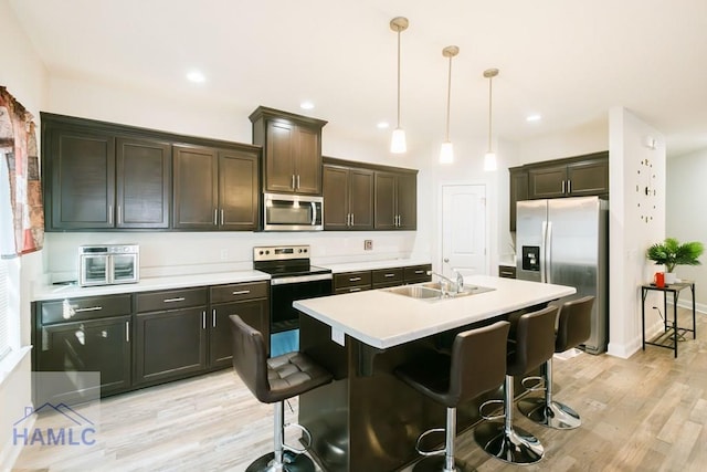 kitchen featuring sink, hanging light fixtures, stainless steel appliances, an island with sink, and a kitchen bar