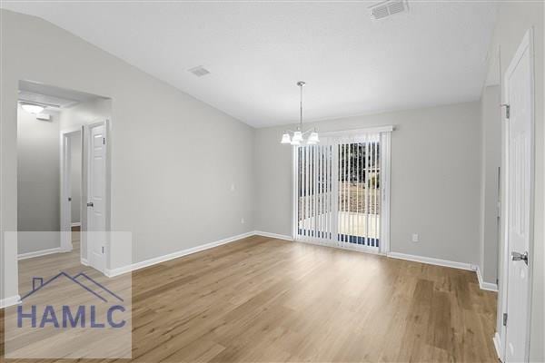 unfurnished dining area featuring a notable chandelier, hardwood / wood-style flooring, and lofted ceiling