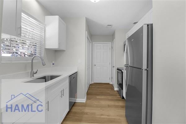 kitchen with sink, stainless steel appliances, white cabinetry, and light wood-type flooring