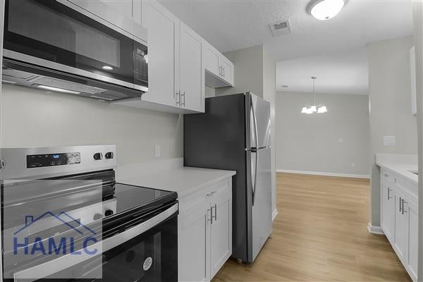 kitchen with appliances with stainless steel finishes, a chandelier, white cabinetry, hanging light fixtures, and light wood-type flooring