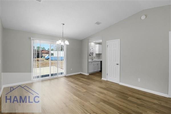 unfurnished dining area featuring wood-type flooring, a chandelier, and vaulted ceiling