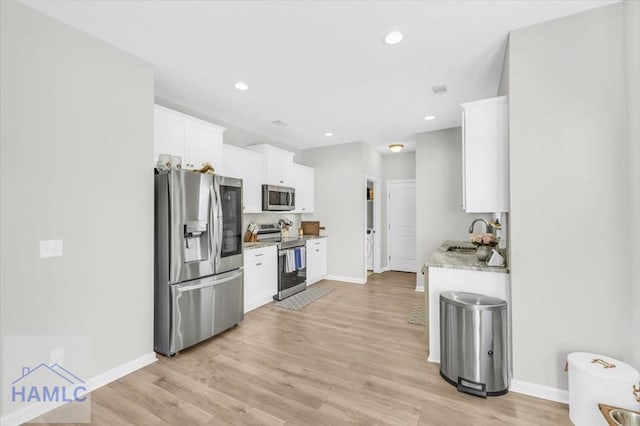 kitchen with light stone countertops, light hardwood / wood-style floors, white cabinetry, appliances with stainless steel finishes, and sink