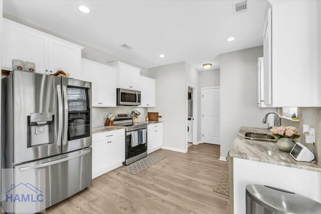 kitchen with light stone counters, light hardwood / wood-style flooring, white cabinets, appliances with stainless steel finishes, and sink