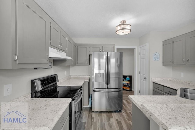 kitchen with gray cabinets, light countertops, under cabinet range hood, light wood-style floors, and appliances with stainless steel finishes