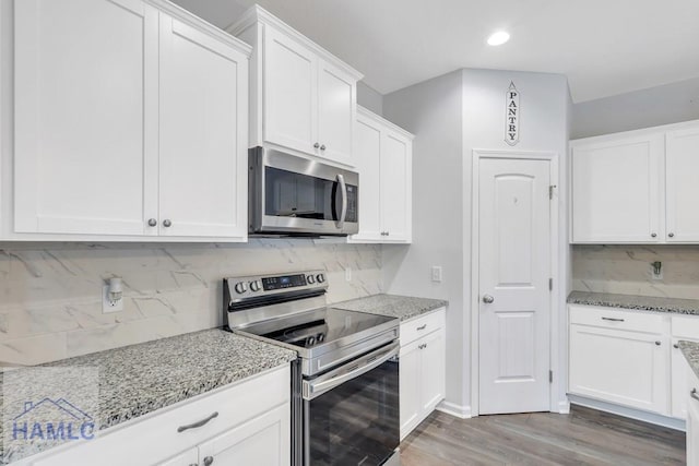 kitchen with white cabinets, light stone counters, stainless steel appliances, and hardwood / wood-style flooring