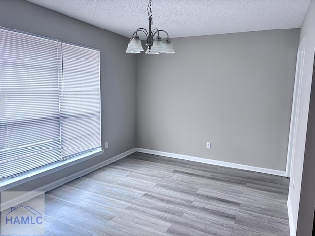 unfurnished room featuring a chandelier, a textured ceiling, and wood-type flooring