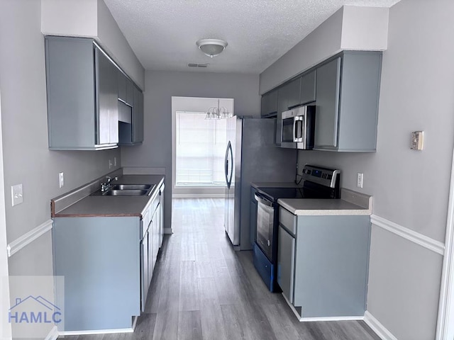 kitchen featuring appliances with stainless steel finishes, a textured ceiling, sink, an inviting chandelier, and light hardwood / wood-style flooring