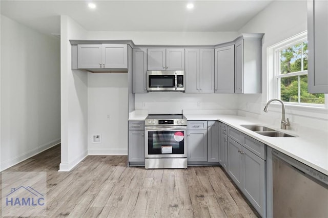 kitchen with appliances with stainless steel finishes, light hardwood / wood-style floors, gray cabinetry, and sink