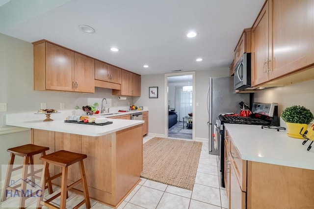 kitchen featuring a breakfast bar, sink, light tile patterned floors, kitchen peninsula, and stainless steel appliances