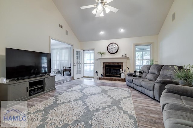 living room featuring ceiling fan, a fireplace, high vaulted ceiling, and light hardwood / wood-style flooring