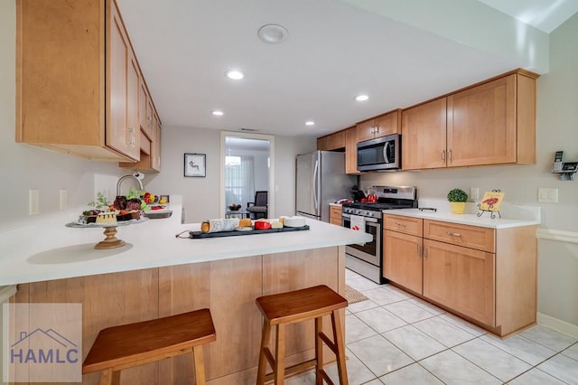 kitchen featuring kitchen peninsula, light brown cabinetry, a breakfast bar, light tile patterned flooring, and appliances with stainless steel finishes