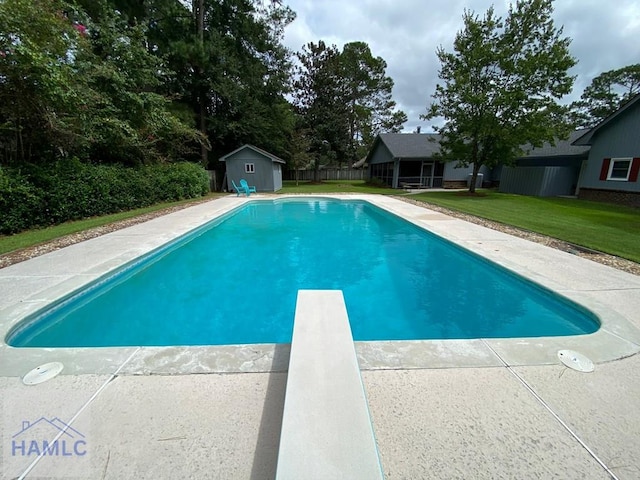 view of swimming pool with a lawn, a storage unit, and a diving board