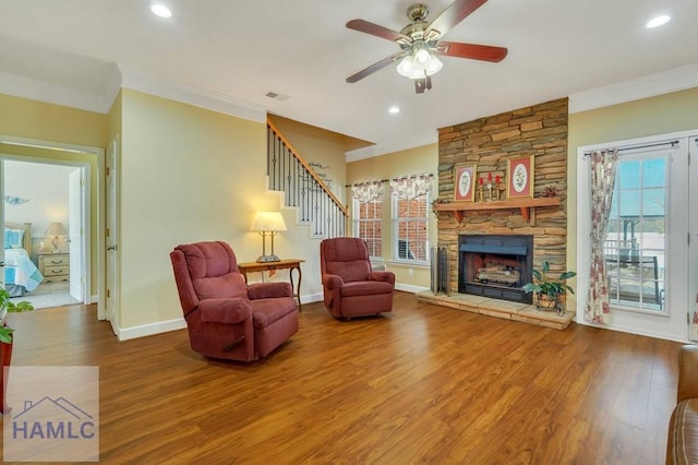 living room featuring hardwood / wood-style floors, crown molding, a stone fireplace, and ceiling fan