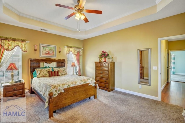 bedroom featuring a raised ceiling, crown molding, and light colored carpet