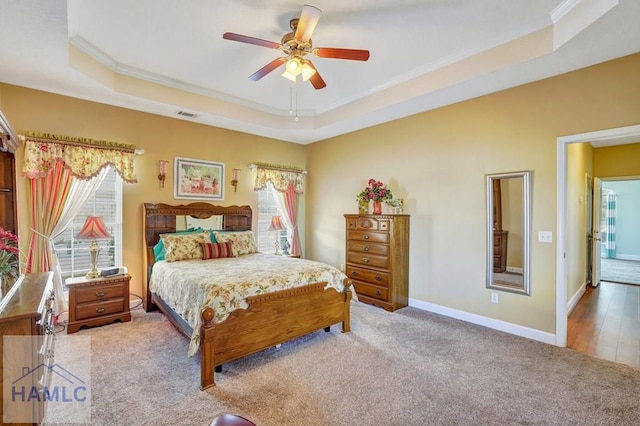 bedroom with ornamental molding, a tray ceiling, and light carpet