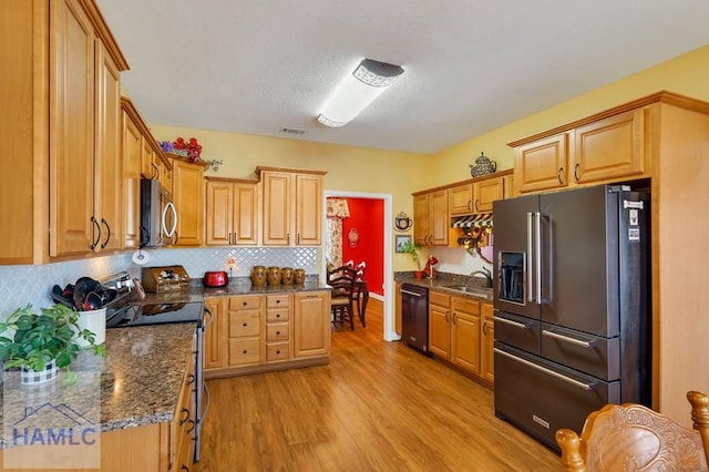 kitchen with sink, light hardwood / wood-style flooring, dark stone countertops, decorative backsplash, and black appliances