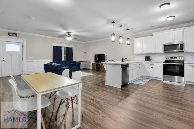 kitchen featuring stainless steel appliances, ornamental molding, hanging light fixtures, and white cabinets