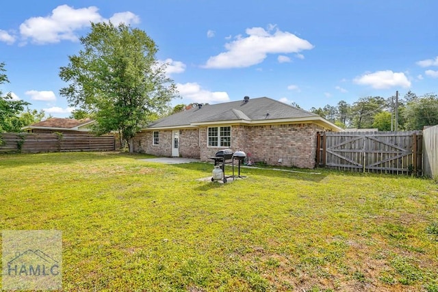 rear view of property featuring a yard, brick siding, a fenced backyard, and a patio area