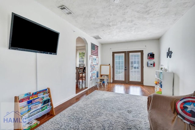 living room with arched walkways, visible vents, french doors, and wood finished floors
