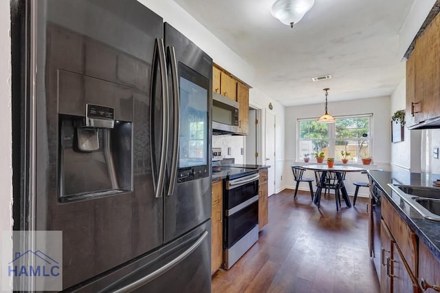 kitchen with pendant lighting, dark countertops, appliances with stainless steel finishes, brown cabinets, and dark wood finished floors