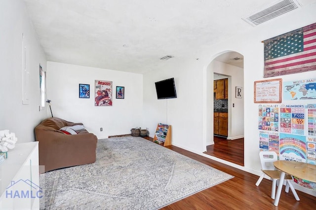 living area featuring visible vents, arched walkways, baseboards, and wood finished floors