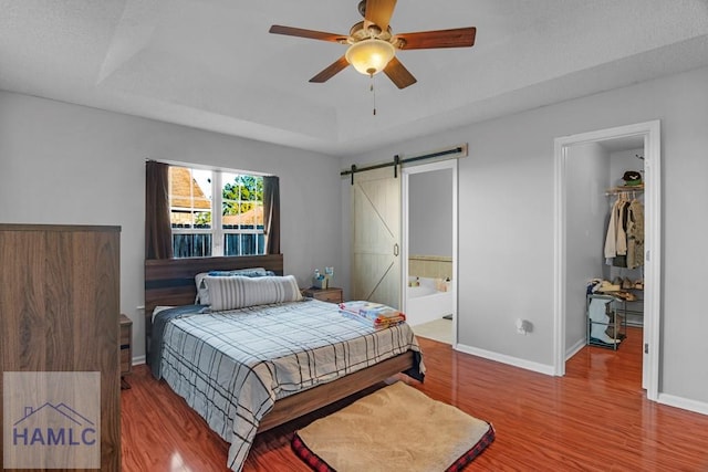 bedroom featuring ceiling fan, ensuite bath, a raised ceiling, and a barn door