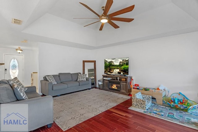 living room with ceiling fan, hardwood / wood-style floors, a raised ceiling, and a fireplace