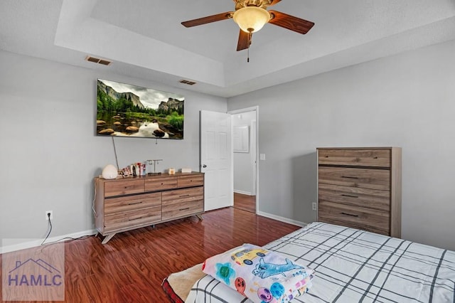 bedroom with a raised ceiling, ceiling fan, and dark hardwood / wood-style flooring