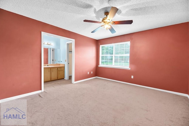 unfurnished bedroom featuring a textured ceiling, light colored carpet, ensuite bath, and ceiling fan