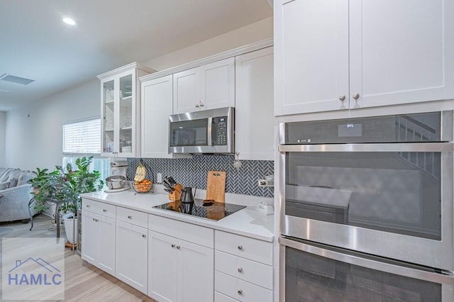 kitchen featuring appliances with stainless steel finishes, white cabinets, tasteful backsplash, glass insert cabinets, and light wood-style floors