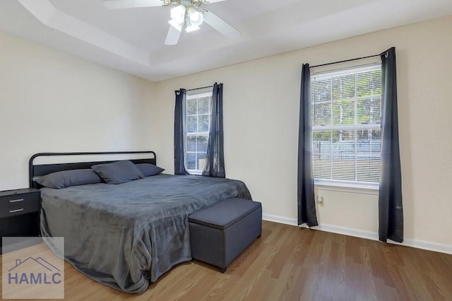 bedroom with ceiling fan, a raised ceiling, and hardwood / wood-style floors