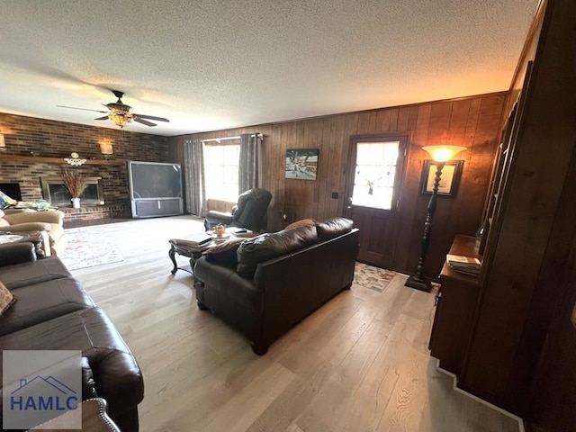 224 Bacon St, Jesup, GA 31545 - living room featuring ceiling fan, a textured ceiling, a brick fireplace, light wood-style floors, and wood walls
