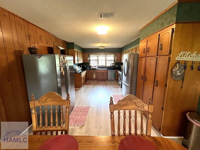 224 Bacon St, Jesup, GA 31545 - kitchen featuring appliances with stainless steel finishes, light wood-style flooring, a textured ceiling, wooden walls, and a sink