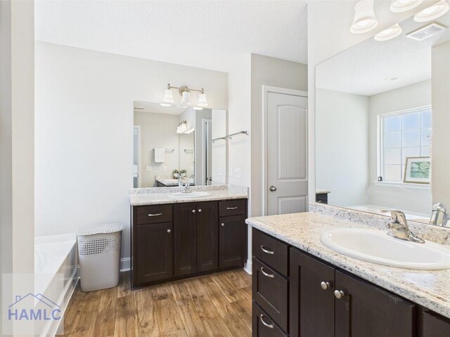bathroom with a bath, visible vents, wood finished floors, two vanities, and a sink