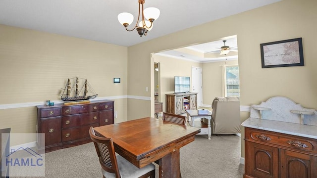dining room with a tray ceiling, ceiling fan with notable chandelier, and light carpet