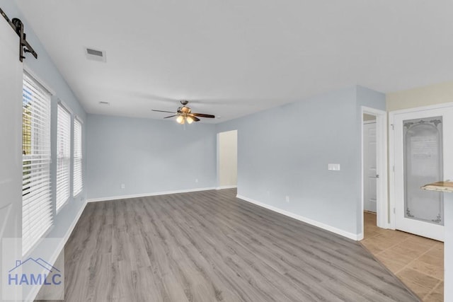 unfurnished room featuring a barn door, ceiling fan, and light hardwood / wood-style flooring