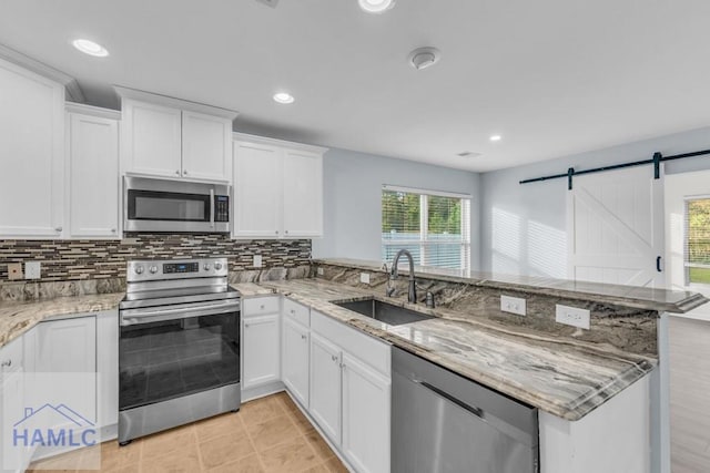 kitchen featuring sink, a barn door, kitchen peninsula, white cabinets, and appliances with stainless steel finishes