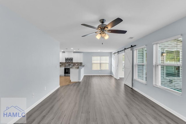 unfurnished living room with a barn door, ceiling fan, and light hardwood / wood-style flooring