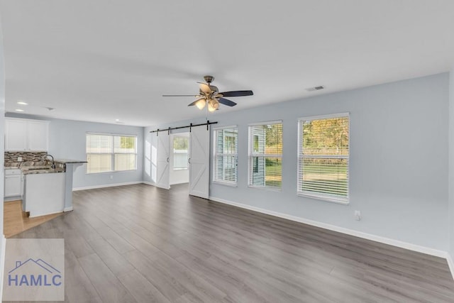 unfurnished living room featuring a barn door, ceiling fan, sink, and light wood-type flooring